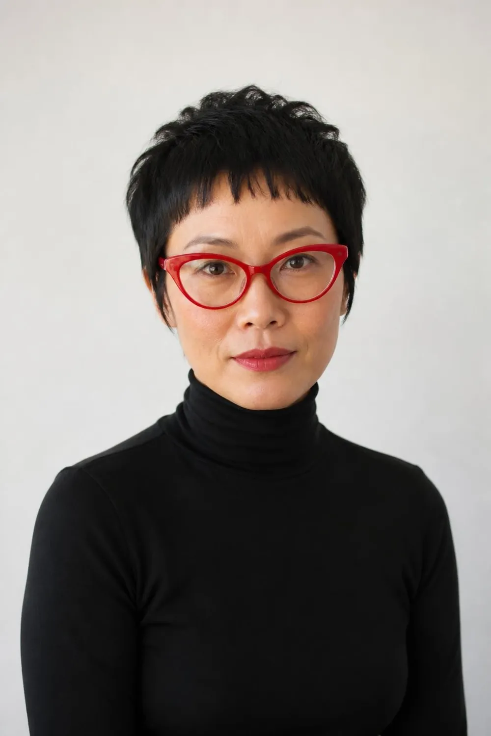 Pixie cut with short baby bangs above bold cat-eye glasses on a woman in her 40s