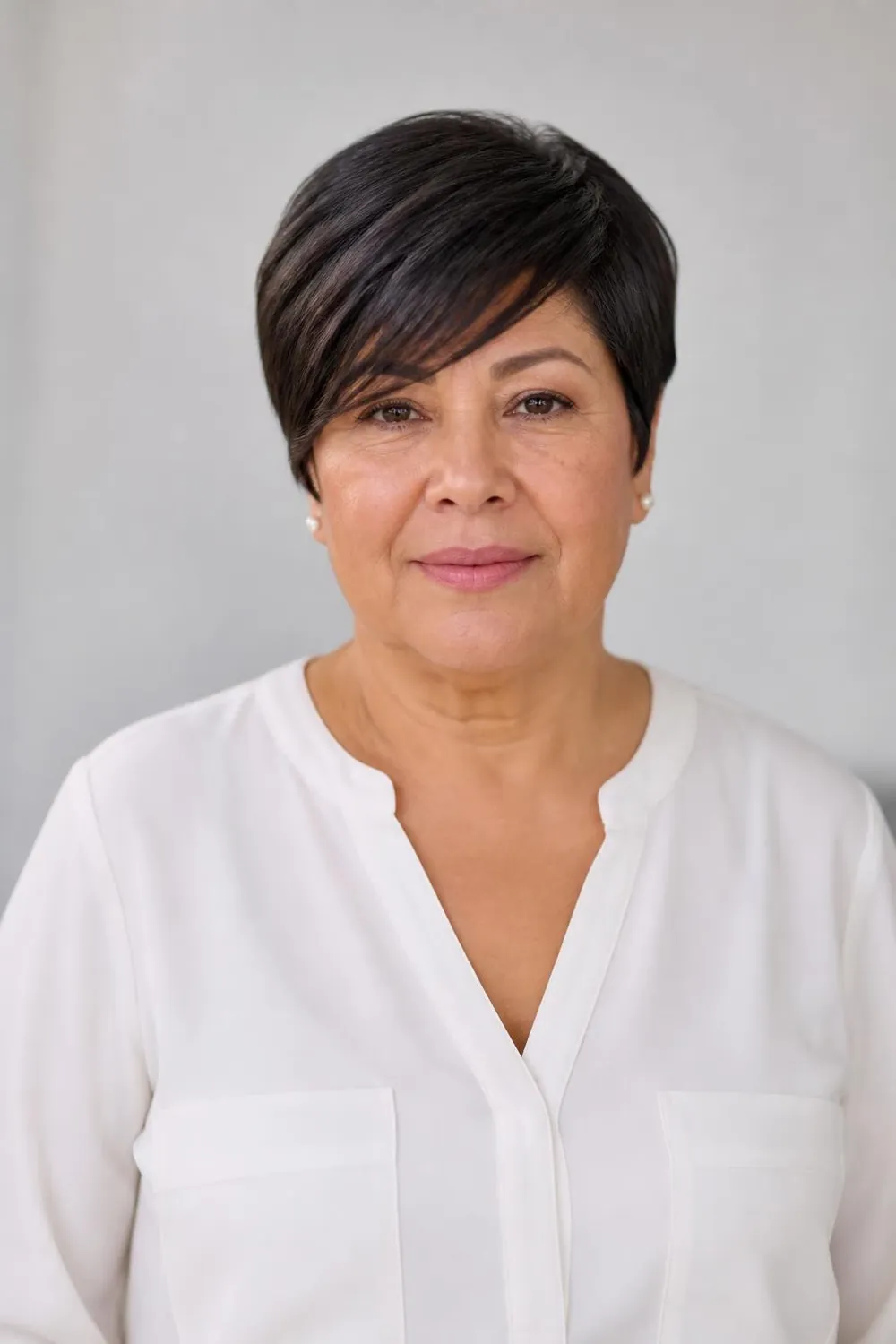 Long pixie with diagonal bangs sweeping across the forehead for a round face over 50